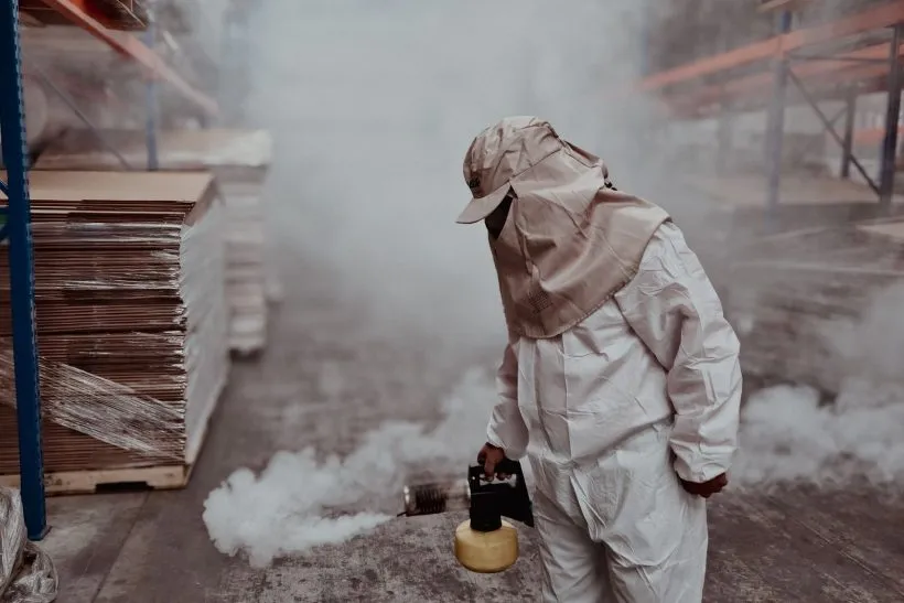 Pest control technician in a full protective suit and hood carrying out a fumigation treatment in a storeroom
