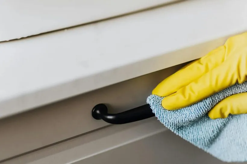 Gloved hand wiping a kitchen cabinet handle, a high-touch surface
