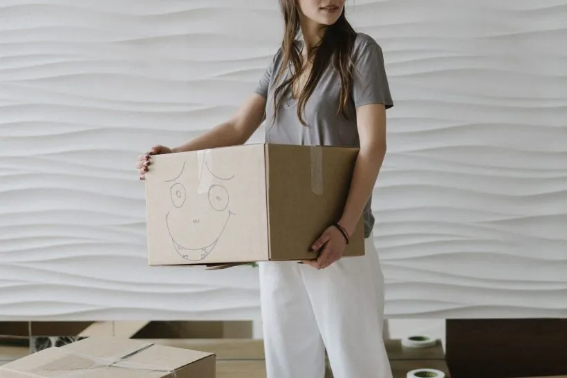 Person carrying a labelled cardboard moving box through an apartment