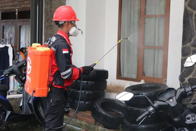 Pest control worker with a backpack sprayer treating the outside of a residential building